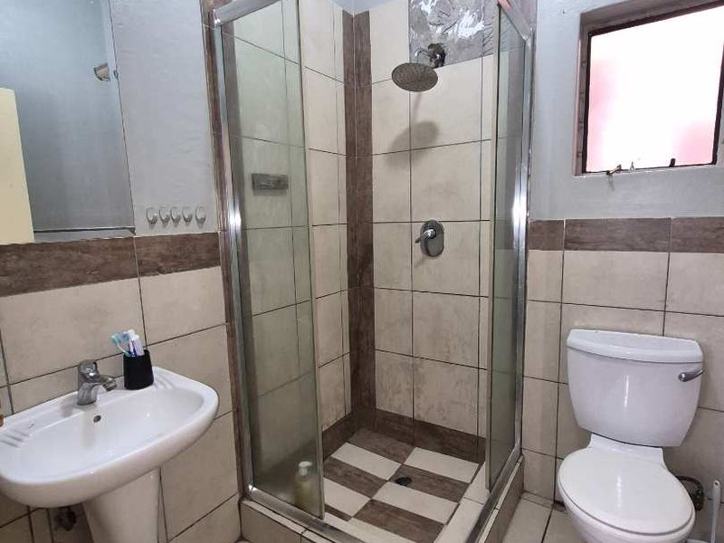 A functional bathroom featuring a pedestal basin, a glass-enclosed shower, and a standard toilet with tiled finishes.