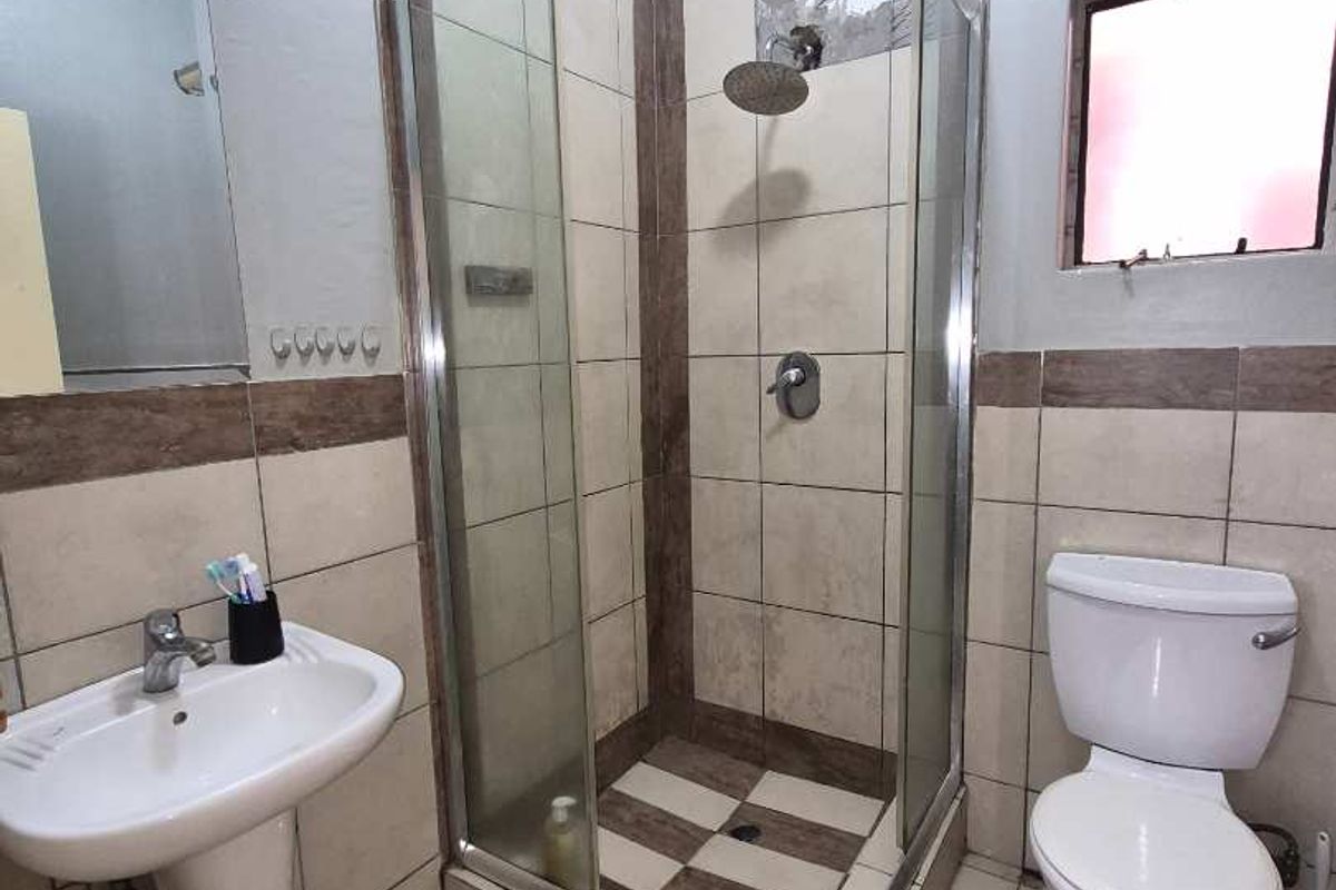 A functional bathroom featuring a pedestal basin, a glass-enclosed shower, and a standard toilet with tiled finishes.