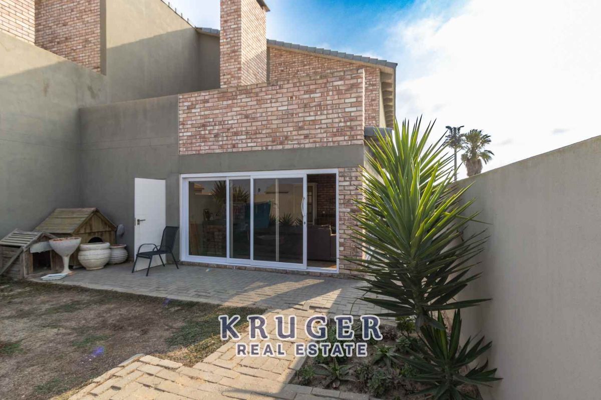 Rear exterior view featuring a paved patio area, sliding glass doors, and brick chimney detail.