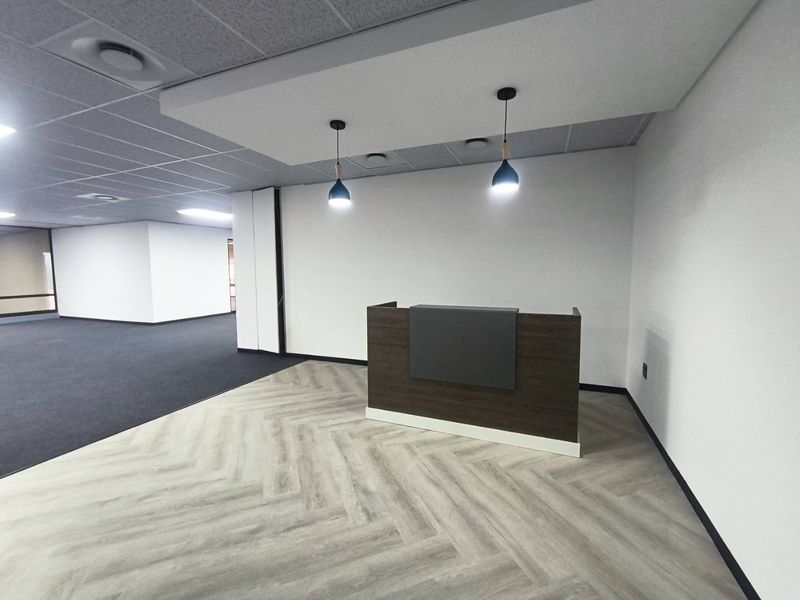 Modern office reception area featuring a built-in desk, herringbone vinyl flooring, and a clean, professional aesthetic with suspended ceiling and pendant lighting.