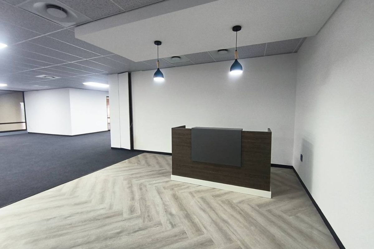 Modern office reception area featuring a built-in desk, herringbone vinyl flooring, and a clean, professional aesthetic with suspended ceiling and pendant lighting.