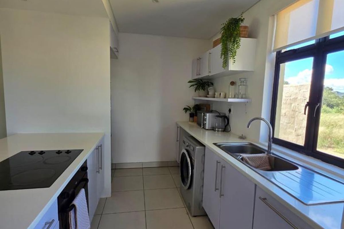 Modern galley-style kitchen featuring sleek cabinetry, integrated oven, electric hob, stainless steel sink, and tiled flooring with ample natural light.