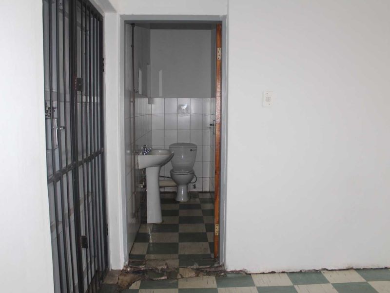 A small, functional bathroom featuring a pedestal basin and toilet, with visible wear to the floor tiles and wall base at the entrance.