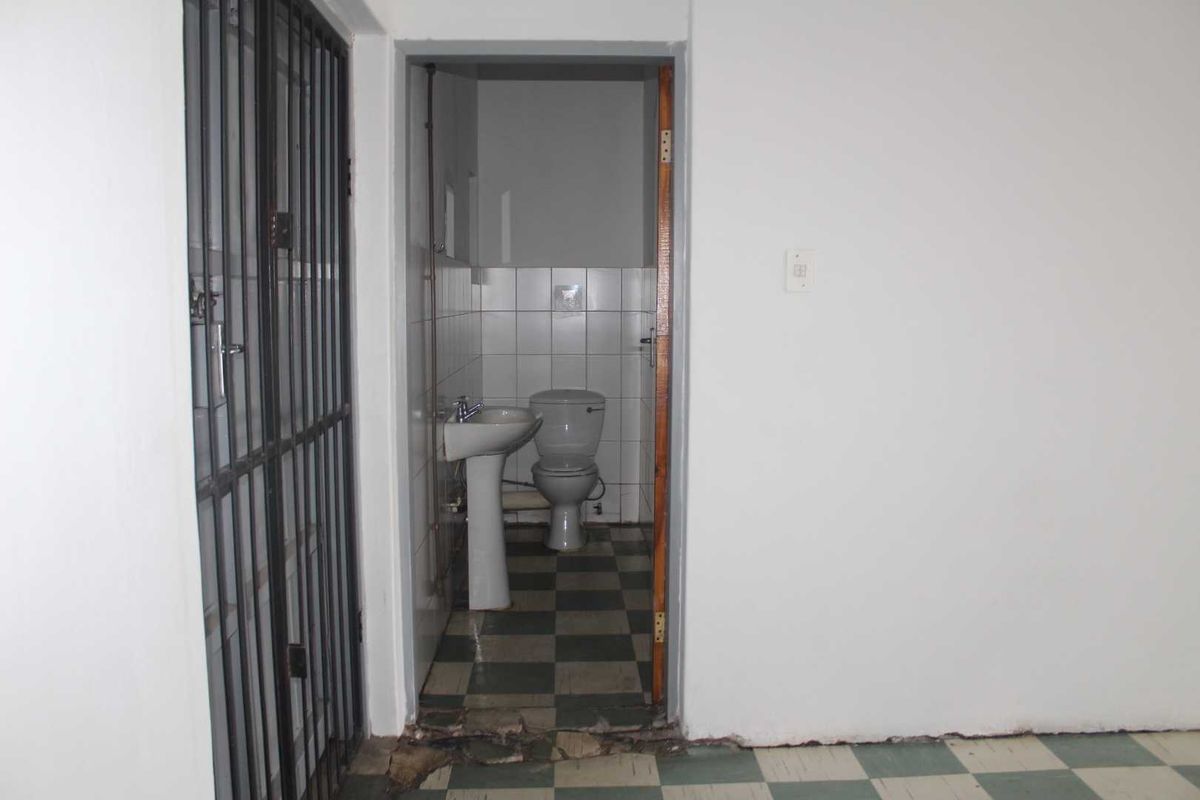 A small, functional bathroom featuring a pedestal basin and toilet, with visible wear to the floor tiles and wall base at the entrance.
