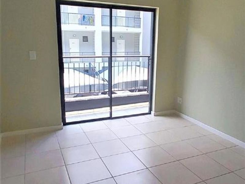An empty living room featuring neutral tiled flooring and a sliding glass door that opens onto a balcony.