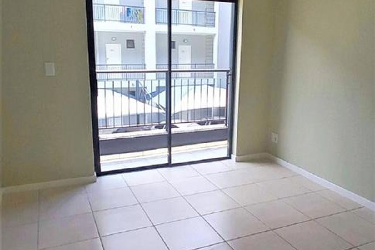 An empty living room featuring neutral tiled flooring and a sliding glass door that opens onto a balcony.