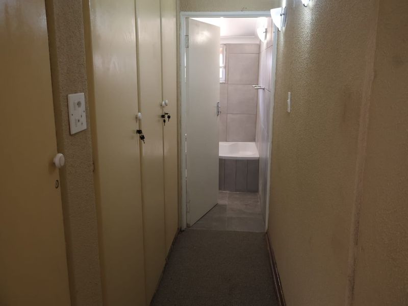 A narrow hallway featuring built-in storage cupboards, leading directly into a bathroom with tiled finishes and a bathtub.