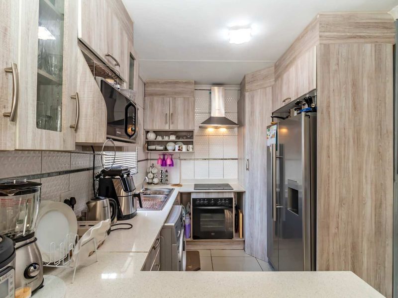 A functional galley-style kitchen featuring light wood-grain cabinetry, stone countertops, a stainless steel extractor fan, and a built-in electric oven and hob.