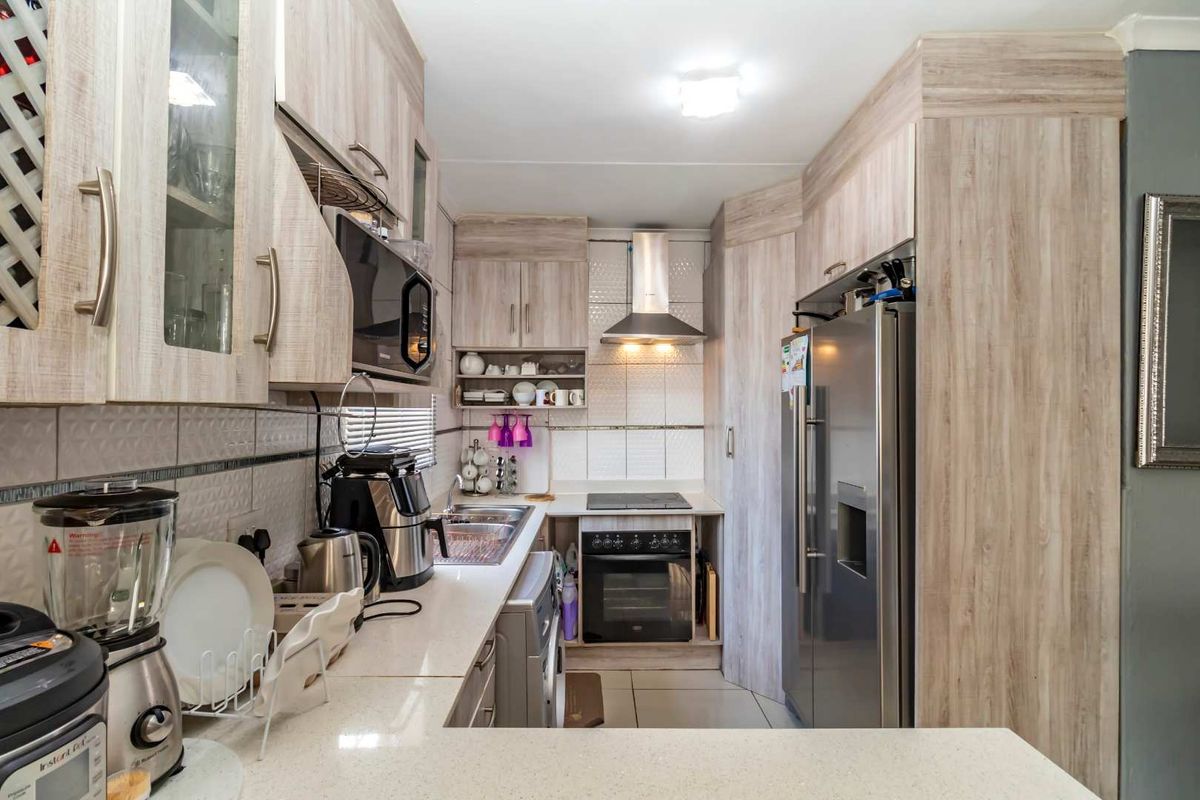 A functional galley-style kitchen featuring light wood-grain cabinetry, stone countertops, a stainless steel extractor fan, and a built-in electric oven and hob.