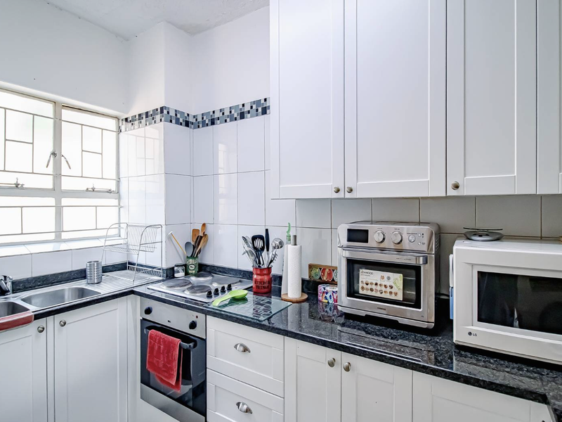 A functional kitchen featuring white cabinetry, dark granite countertops, a built-in oven, electric hob, and tiled backsplash with a window for natural light.