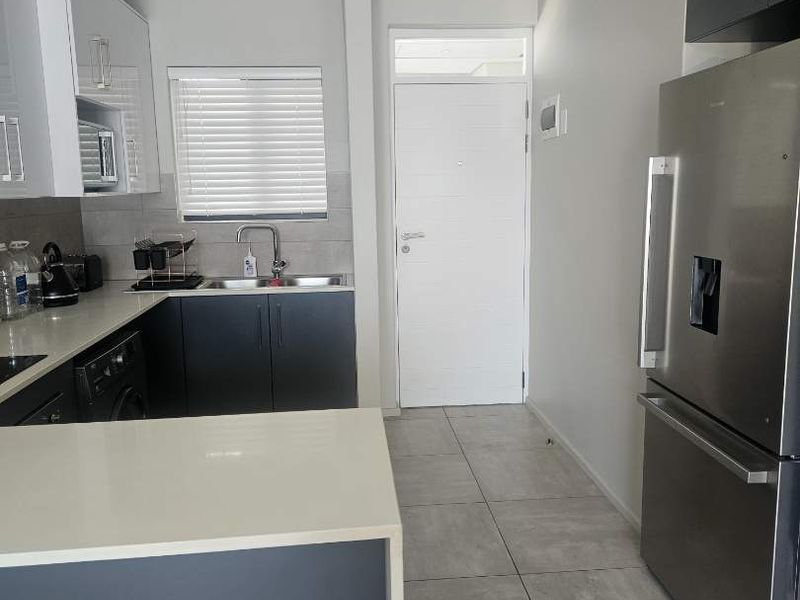 Modern kitchen featuring sleek dark and white cabinetry, quartz countertops, tiled flooring, and a functional layout with integrated space for appliances.