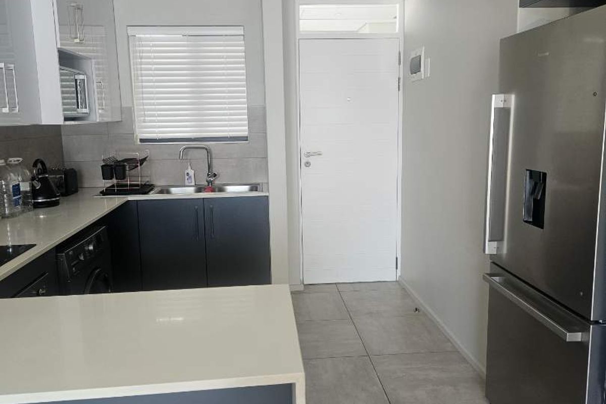 Modern kitchen featuring sleek dark and white cabinetry, quartz countertops, tiled flooring, and a functional layout with integrated space for appliances.
