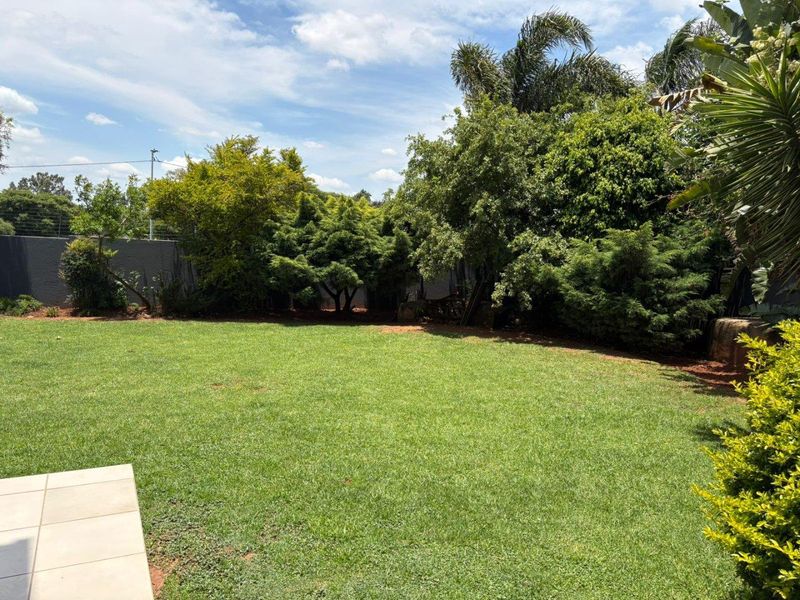 A well-maintained private garden featuring a lush green lawn, mature trees, and secure perimeter walling with electric fencing.
