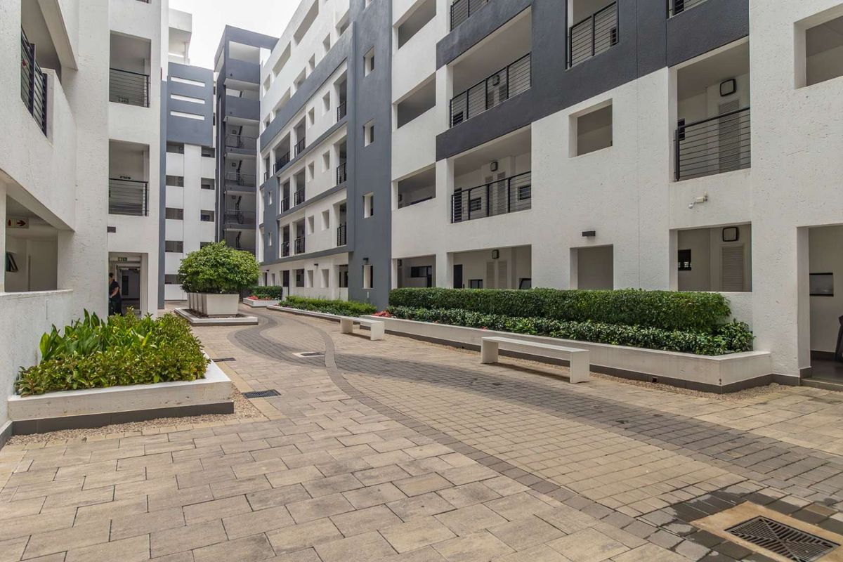 A well-maintained paved courtyard area between apartment blocks featuring raised garden beds, built-in concrete seating, and modern architectural finishes.