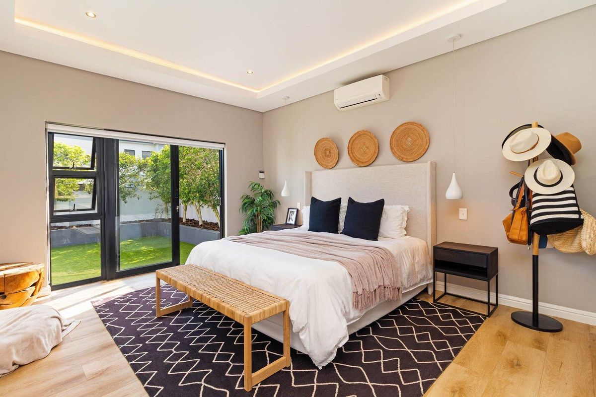 A bright and modern bedroom featuring recessed ceiling lighting, a wall-mounted air conditioning unit, and large sliding glass doors opening to a private garden.