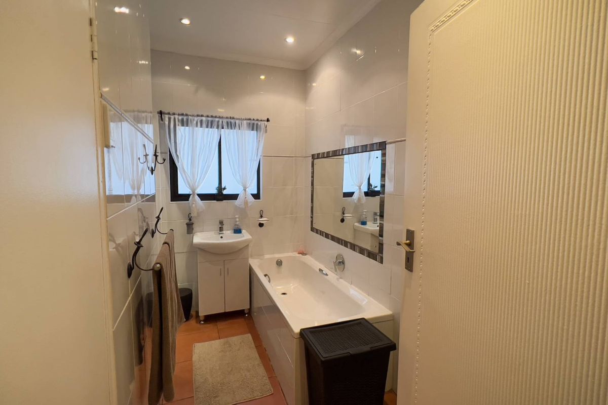 A functional bathroom featuring a built-in bathtub, pedestal washbasin, and tiled wall finishes with recessed lighting.