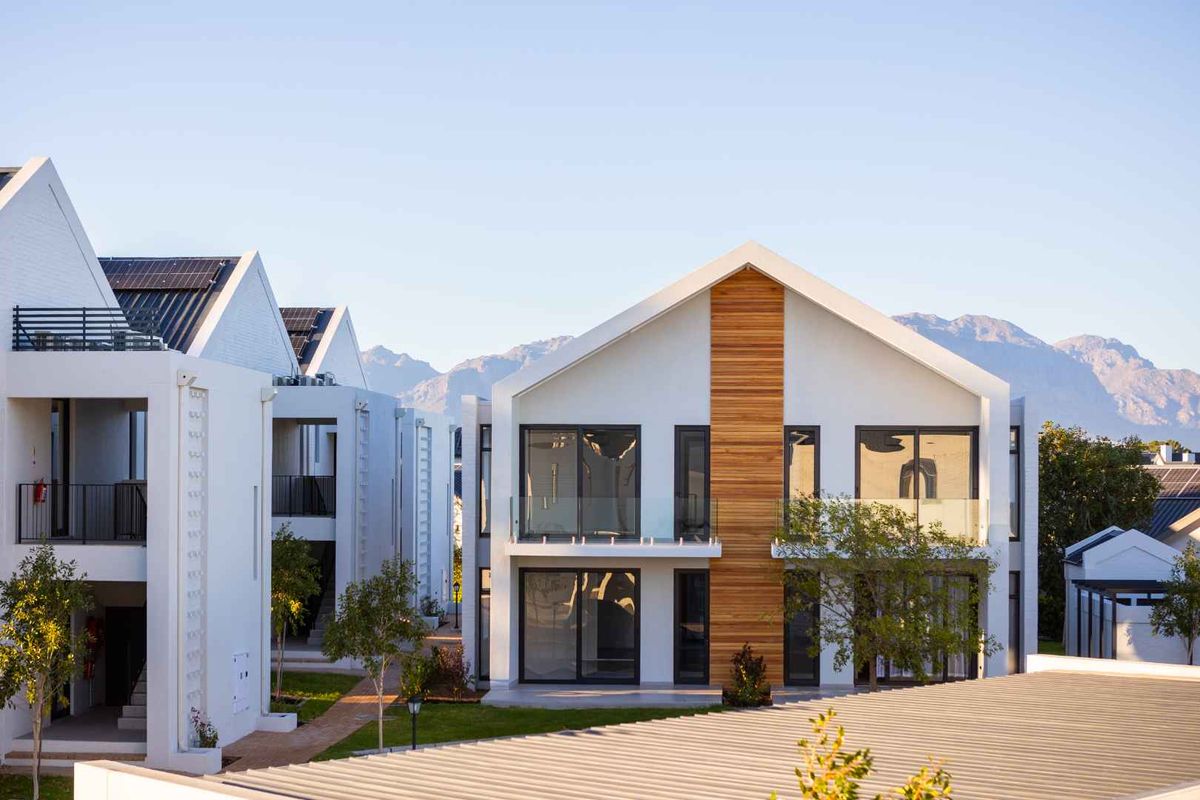 Modern apartment complex featuring contemporary architecture with timber accents, glass balustrades, and solar panels, set against a scenic mountain backdrop.