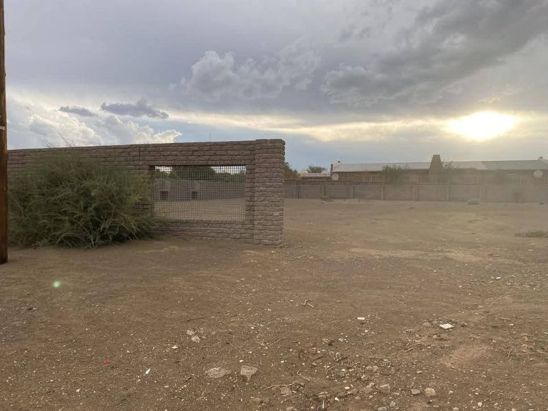 A vacant residential plot featuring a masonry boundary wall with wire mesh fencing under a cloudy sky.