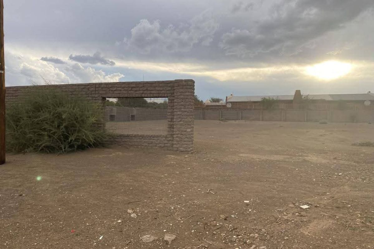 A vacant residential plot featuring a masonry boundary wall with wire mesh fencing under a cloudy sky.