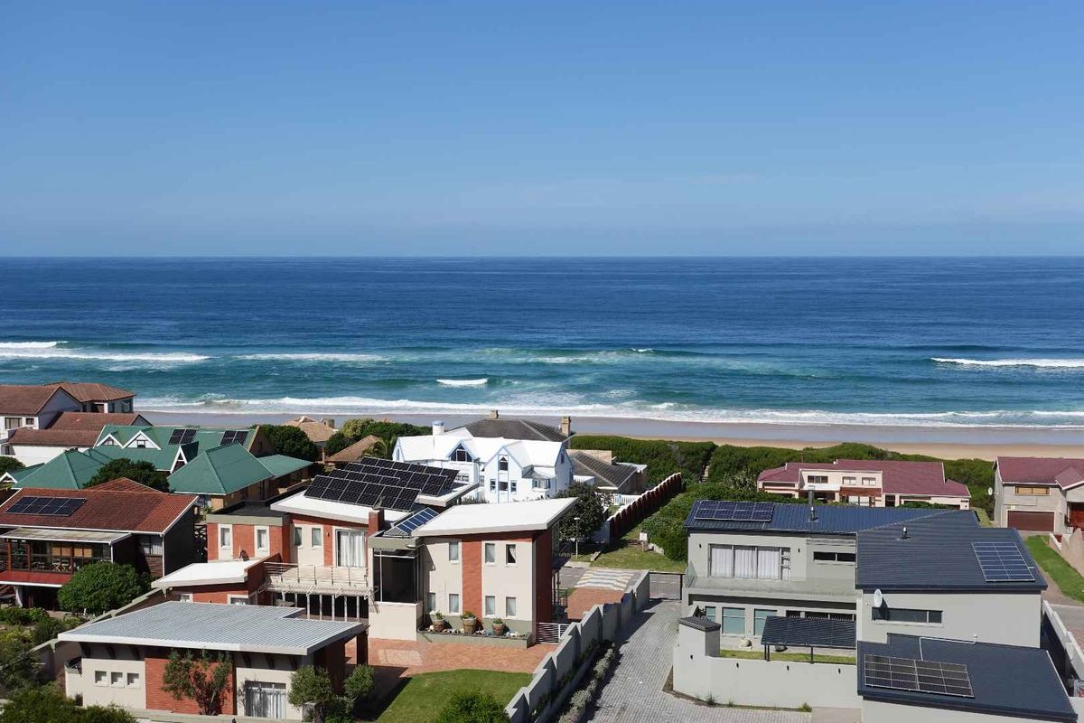 An aerial view of a coastal residential neighborhood featuring homes with solar panels, paved driveways, and direct proximity to the ocean.