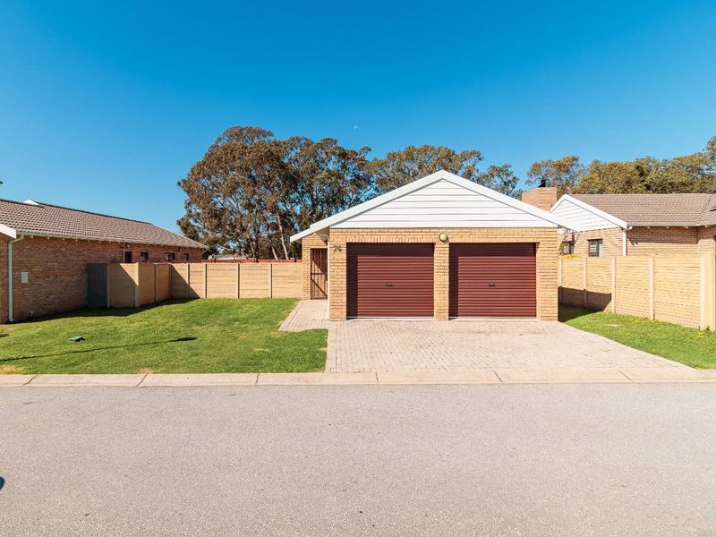 Front view of a residential property featuring a double garage with roller doors, a paved driveway, and a neat front garden with perimeter walling.