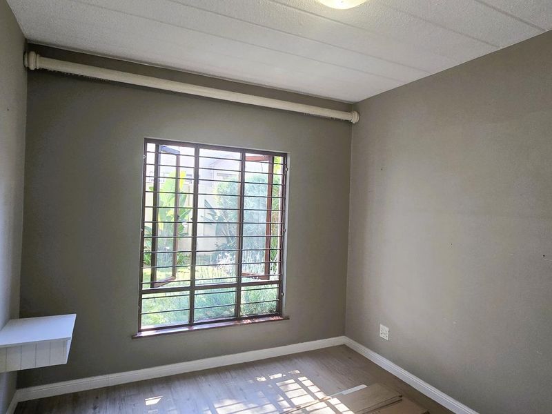 An empty bedroom featuring laminate flooring, security bars on the window, and a built-in wall shelf.