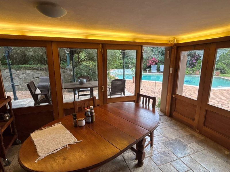 A bright living area featuring timber-framed glass doors that open onto a patio and pool area, complemented by stone tile flooring and ambient lighting.