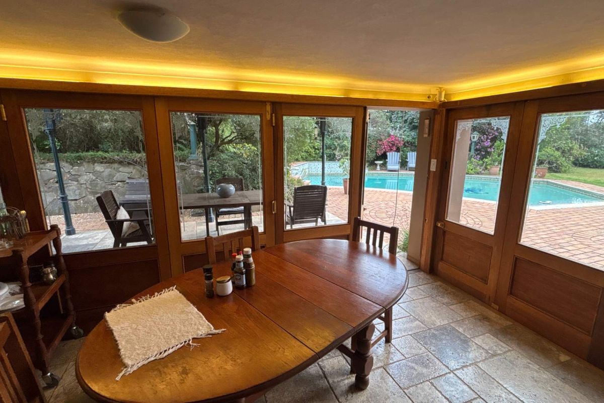 A bright living area featuring timber-framed glass doors that open onto a patio and pool area, complemented by stone tile flooring and ambient lighting.