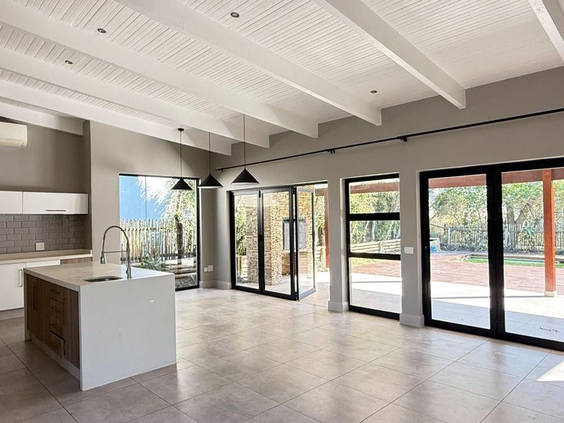 Spacious open-plan kitchen and living area featuring a central island, exposed beam ceilings, and large bi-fold doors opening to an outdoor patio.