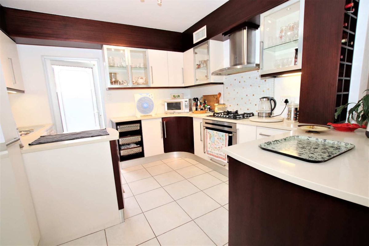Modern kitchen featuring white cabinetry with dark wood accents, stone countertops, a gas hob, stainless steel extractor fan, and tiled flooring.