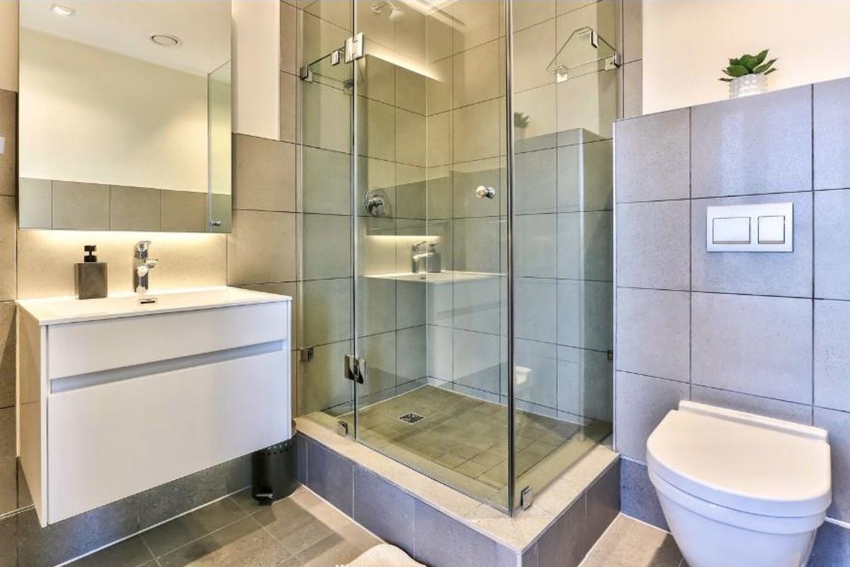 Modern bathroom featuring a wall-mounted vanity, glass-enclosed shower with tiled surround, and a wall-hung toilet with integrated flush plate.