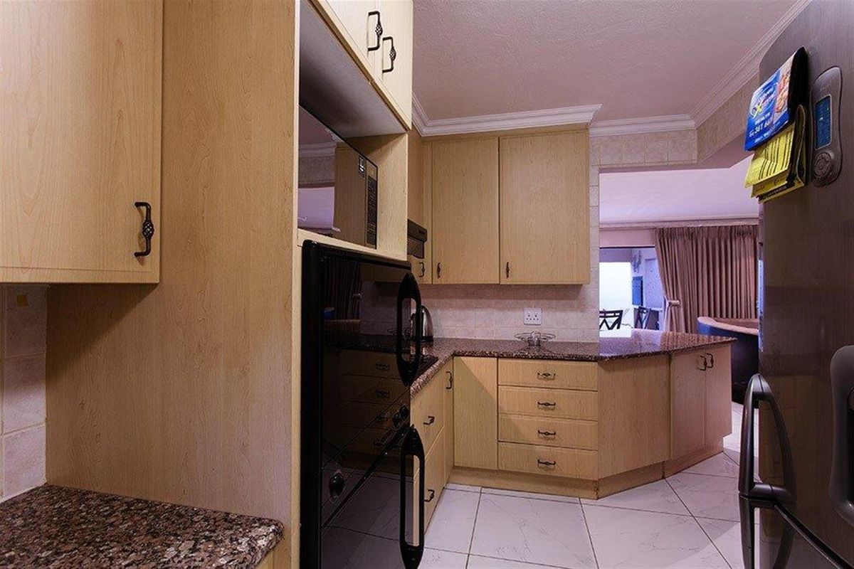 A functional kitchen featuring light wood cabinetry, granite countertops, and tiled flooring, with an open-plan layout flowing into the adjacent living area.