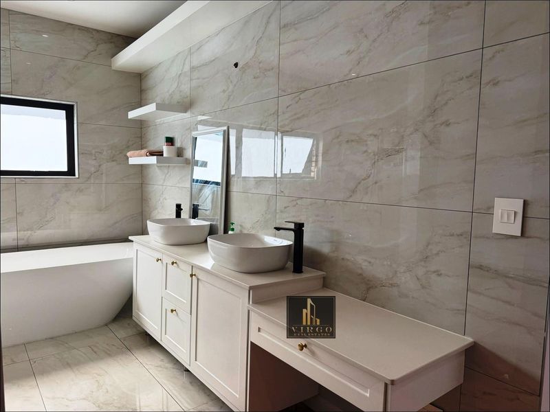 Modern bathroom featuring a double vanity with vessel sinks, black fixtures, a freestanding bathtub, and elegant marble-look wall tiling.