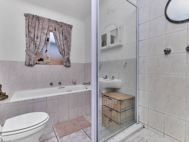 A functional bathroom featuring a built-in bathtub, separate shower enclosure, pedestal basin, and toilet with neutral wall and floor tiling.