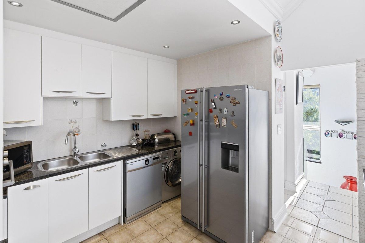 A functional kitchen featuring white cabinetry, granite countertops, a double sink, and integrated space for laundry appliances.