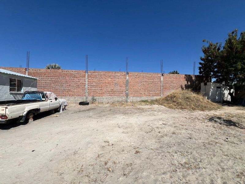 A large, undeveloped rear yard area featuring an unfinished brick boundary wall with exposed rebar, offering significant potential for landscaping or further development.