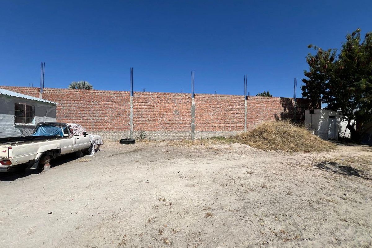 A large, undeveloped rear yard area featuring an unfinished brick boundary wall with exposed rebar, offering significant potential for landscaping or further development.
