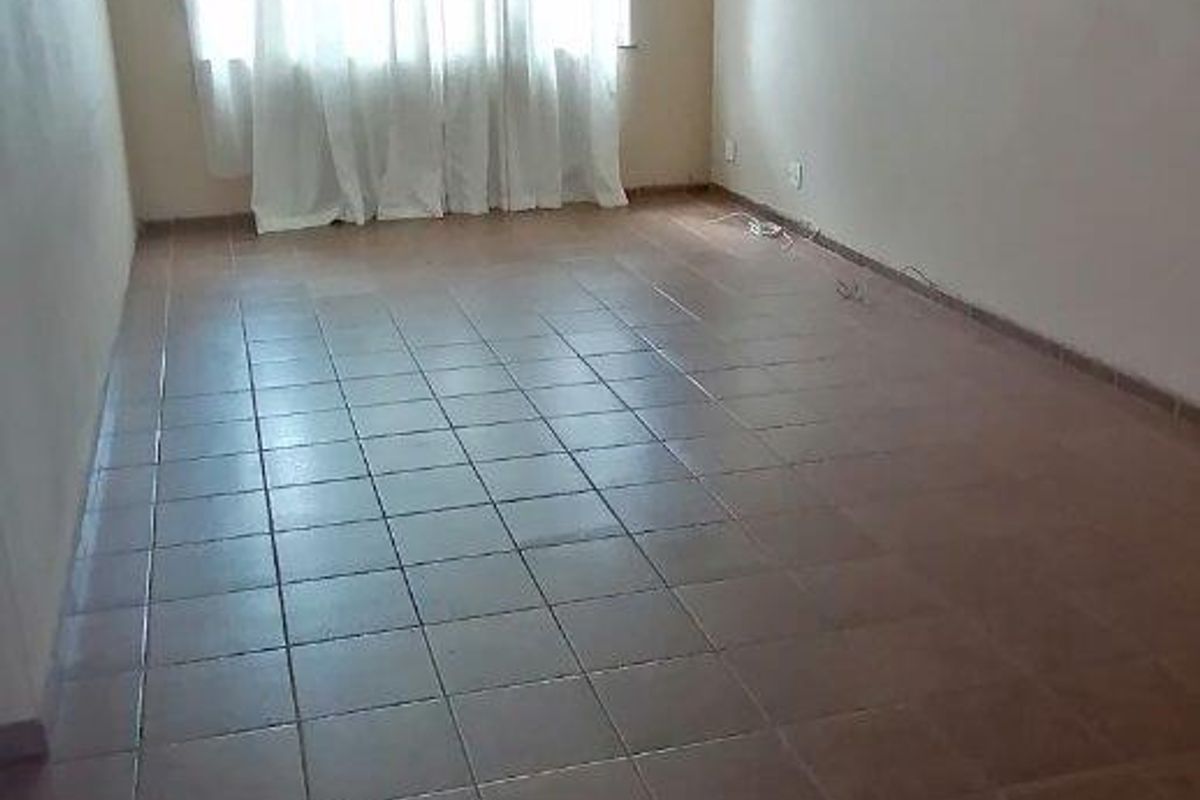 An empty living room featuring ceramic floor tiles and natural light from a large window, ready for renovation or staging.