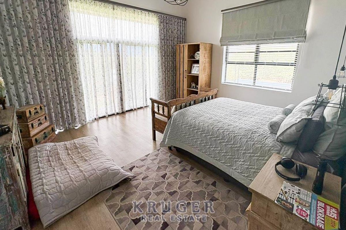 A well-lit bedroom featuring laminate flooring, large sliding glass doors with floor-to-ceiling curtains, and a window with a fitted roller blind.