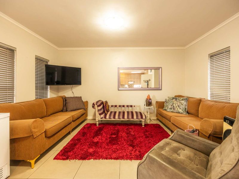A spacious living room featuring tiled flooring, neutral wall tones, and dual windows fitted with venetian blinds.