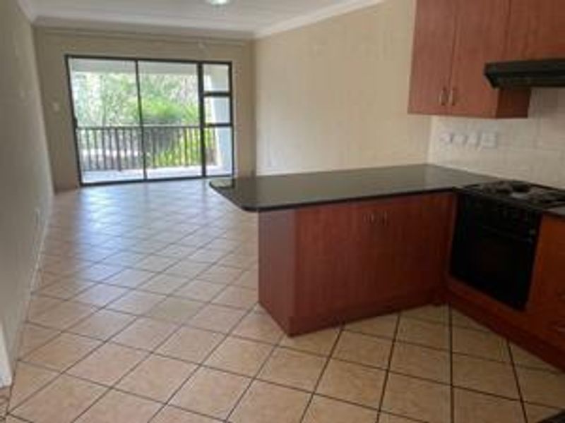 Open-plan kitchen and living area featuring tiled floors, built-in cabinetry with granite countertops, and sliding door access to a balcony.