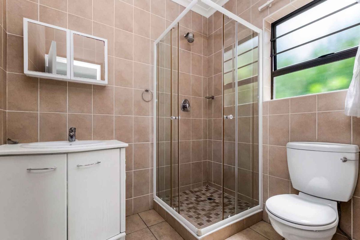 A functional bathroom featuring a glass-enclosed shower, a vanity with integrated basin, and neutral wall tiling.