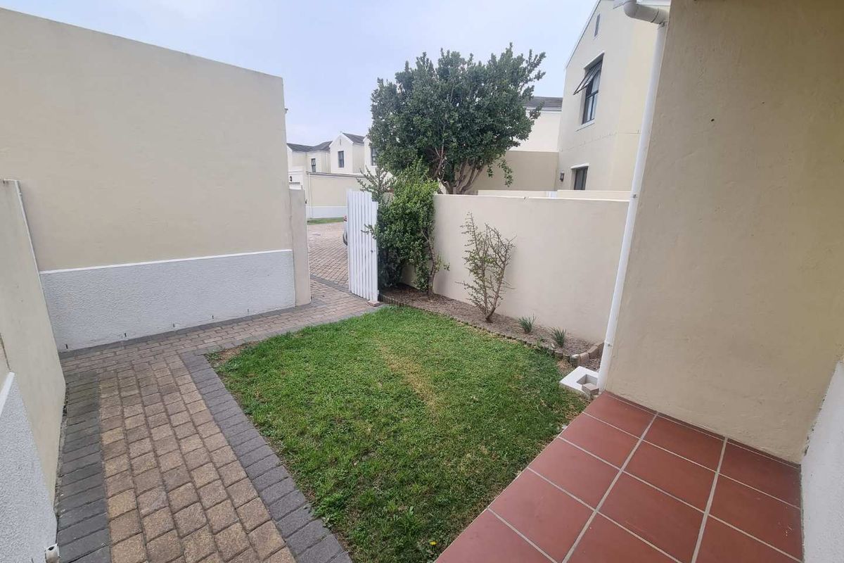 A private rear courtyard featuring a small lawn, paved walkway, and a tiled patio area enclosed by boundary walls.