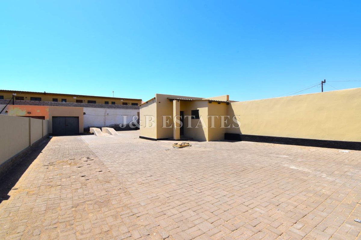 Exterior view of a commercial property featuring a paved courtyard, perimeter boundary walls, and a small detached structure.