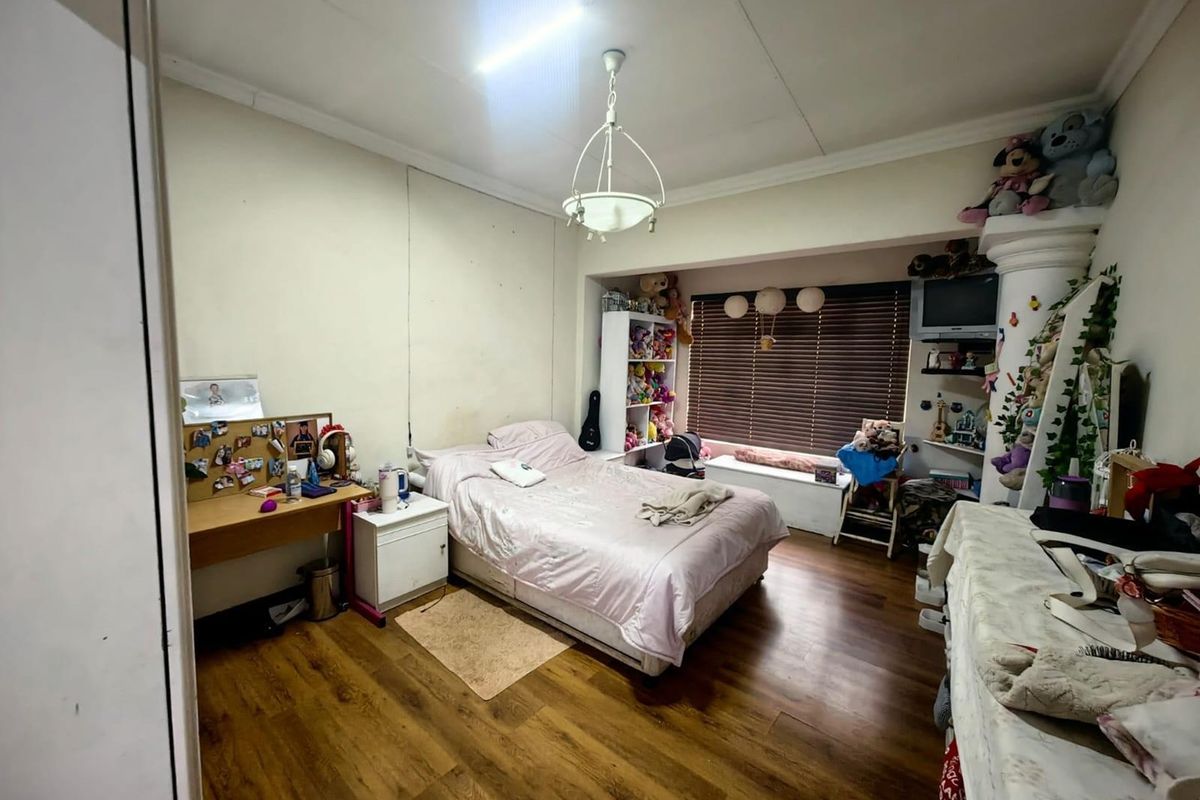 A bedroom featuring laminate flooring, a built-in window seat with venetian blinds, and a decorative column, offering a functional space with potential for cosmetic updates.