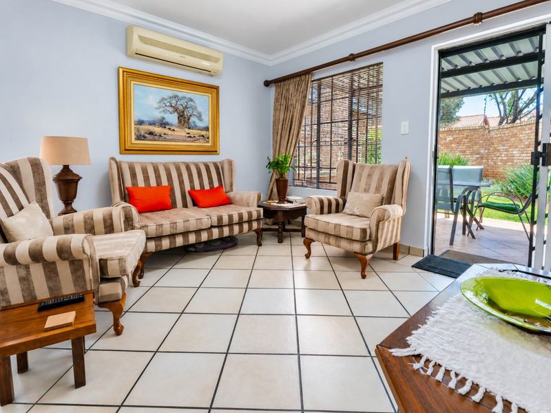 A well-maintained living room featuring tiled flooring, crown molding, and a split-system air conditioner, with direct access to an outdoor patio area.