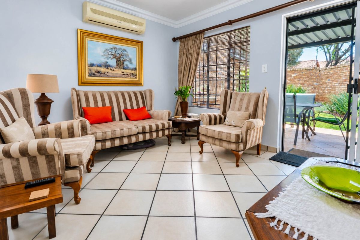 A well-maintained living room featuring tiled flooring, crown molding, and a split-system air conditioner, with direct access to an outdoor patio area.