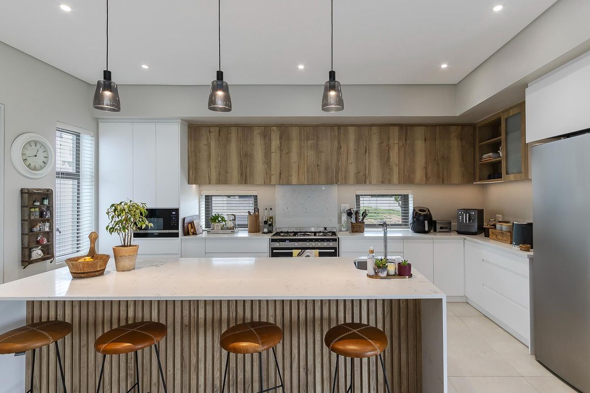 Modern kitchen featuring a large central island with stone countertops, sleek white cabinetry, wood-grain upper cabinets, and integrated stainless steel appliances.