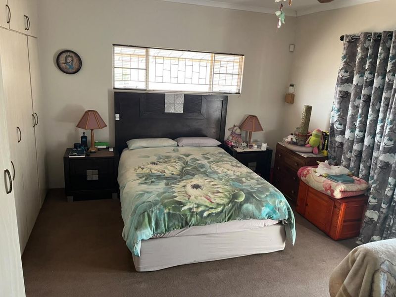 A standard bedroom featuring built-in cupboards and security burglar bars on the window, providing a functional and lived-in space.