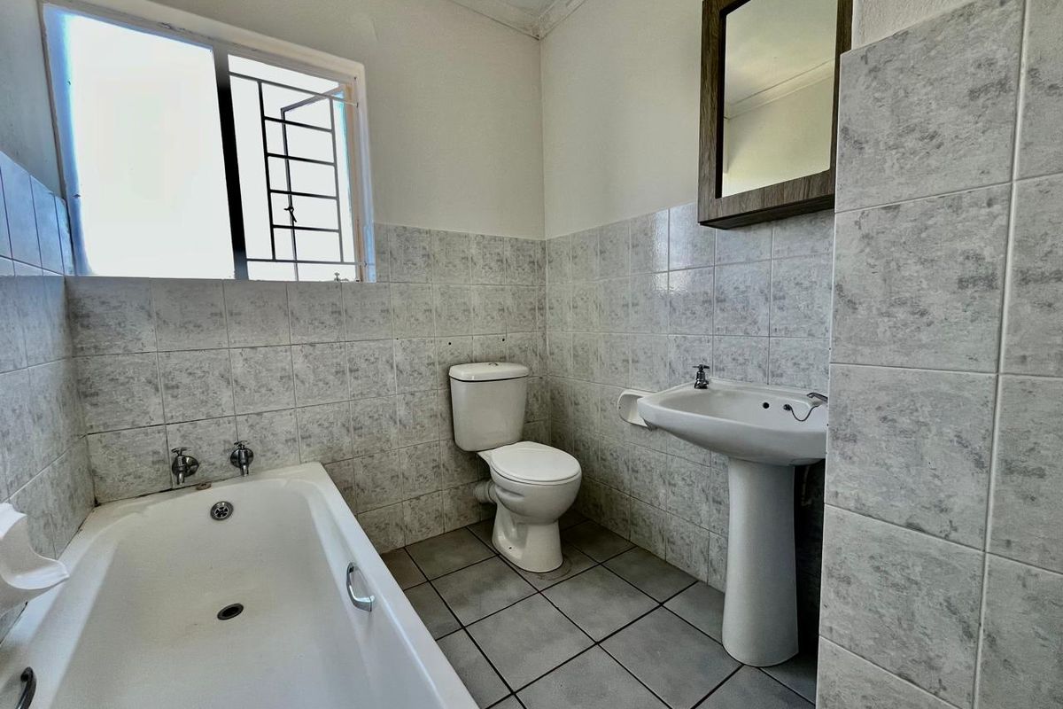 A functional bathroom featuring a bathtub, pedestal basin, and toilet, finished with neutral ceramic wall and floor tiles.